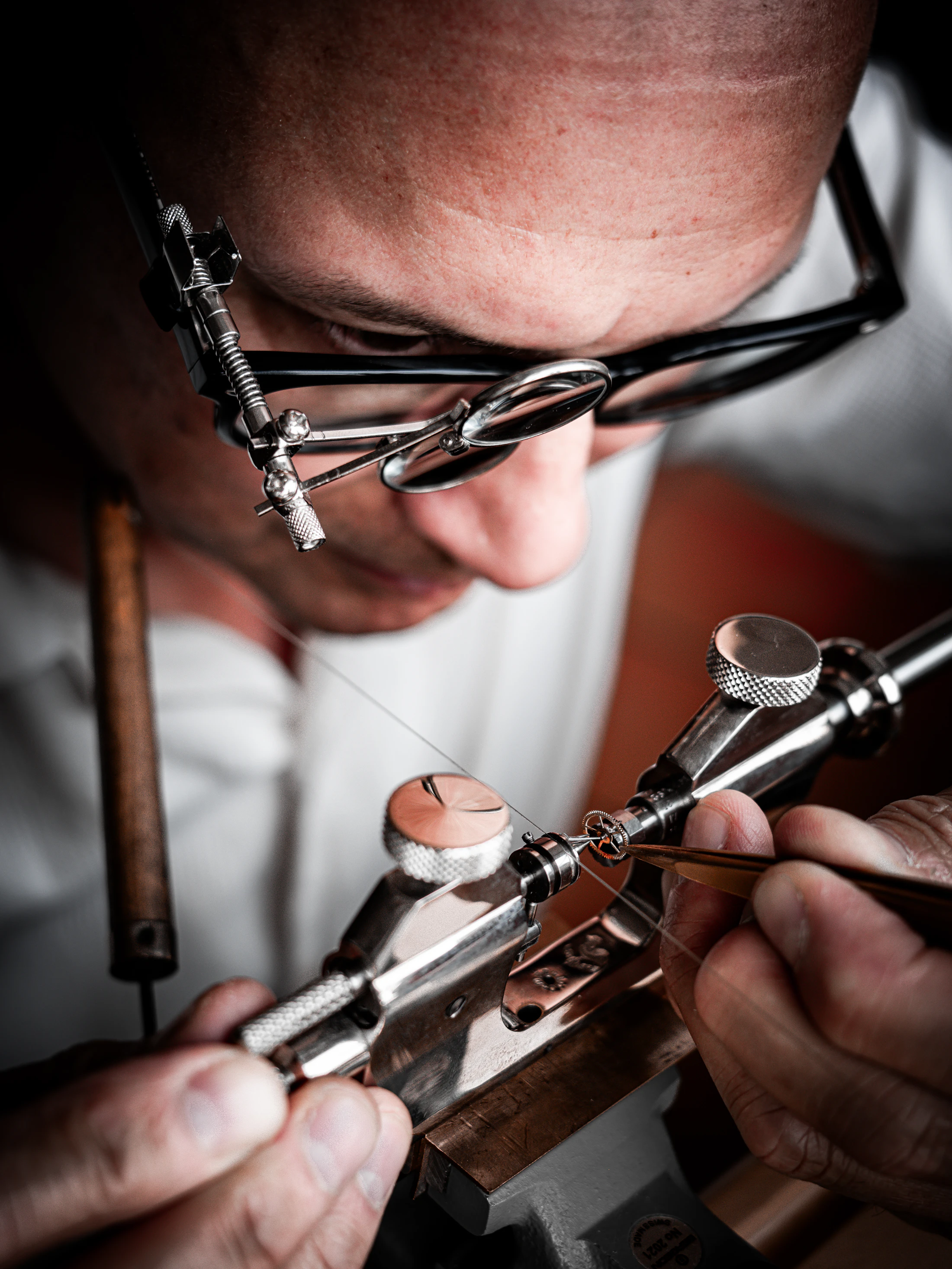 A watchmaker setting a balance with fine tweezers on a staking tool.
