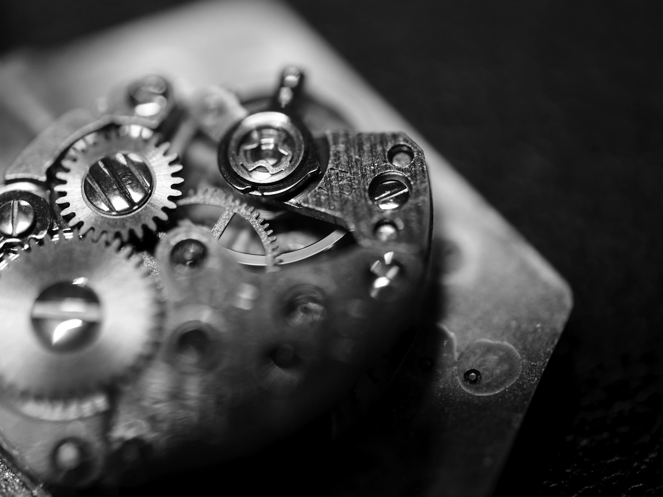 An old movement on a dark bench, its wheels and balance catching a single light.