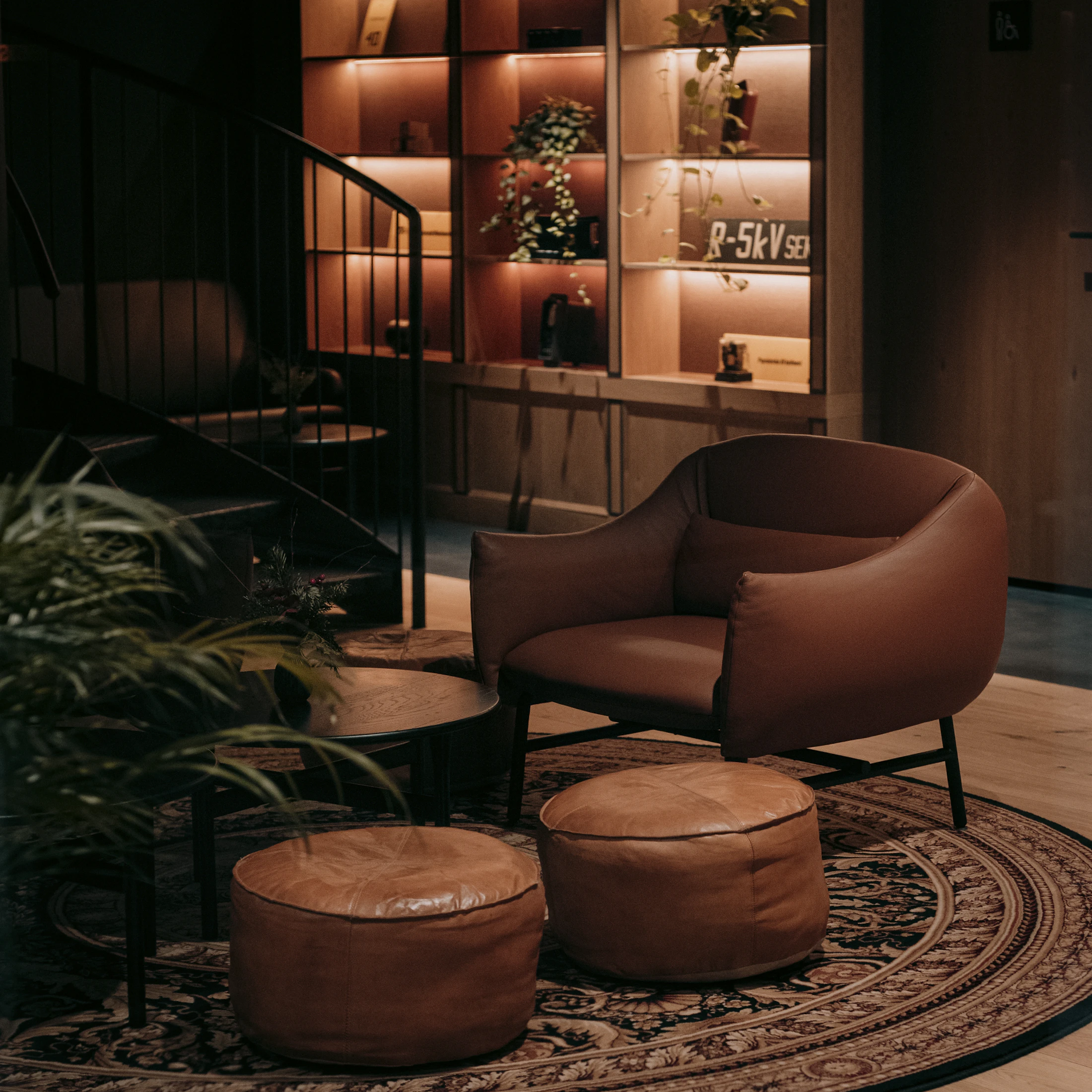 A leather armchair and two poufs on an old rug, in a warm, dimly lit room.